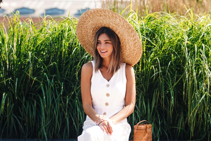 Woman sitting in front of long grass with straw hat