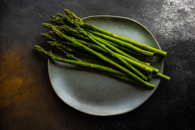 Loose raw asparagus on grey plate with copy space
