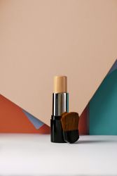 Concealer stick and make up brush on modern background