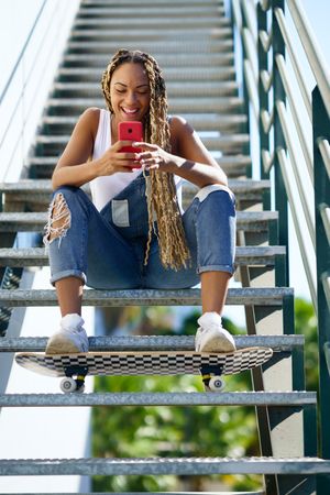 Happy female skater checking phone on stairs