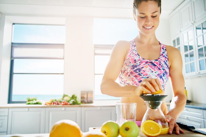 Fit woman in sports bra juicing an orange
