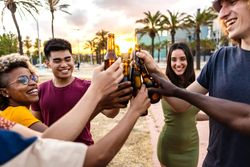 Happy multi-ethnic friends and clinking their beer bottles together outside at dusk