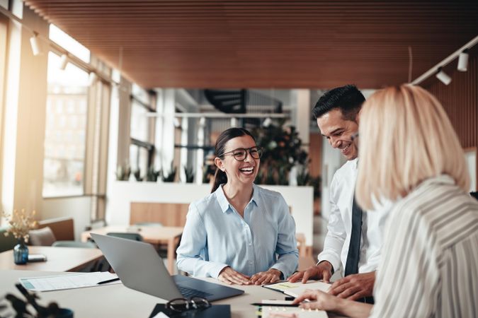 Business people smiling and laughing around a table and laptop