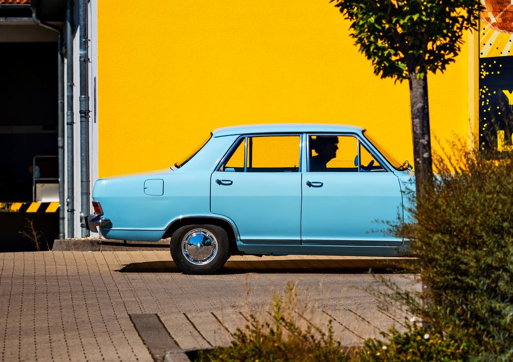Sky blue retro car against a bright yellow wall. Color contrast.