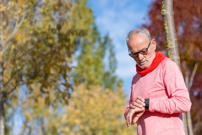 Older male looking down at watch in autumn park