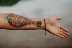 Crop tattooed arm over calm water