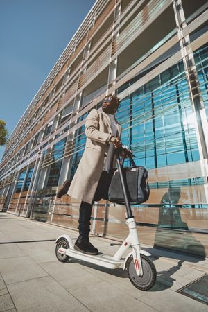 Young Black businessman with handbag on scooter on street