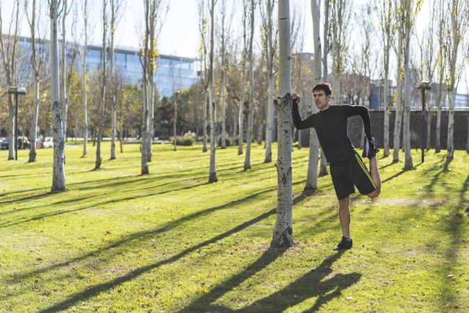 man leaning against a tree stretching his quadriceps