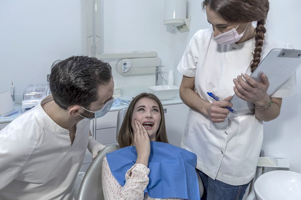 Teenage girl with tooth pain sitting to dental chair