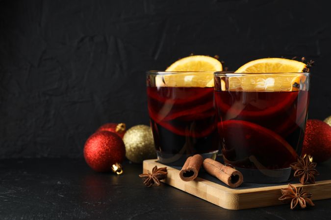 Glasses of tasty mulled wine and christmas baubles on dark background, space for text