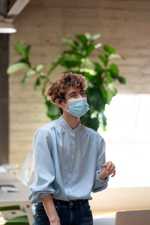 Person standing and smiling wearing a face mask in a bright modern office