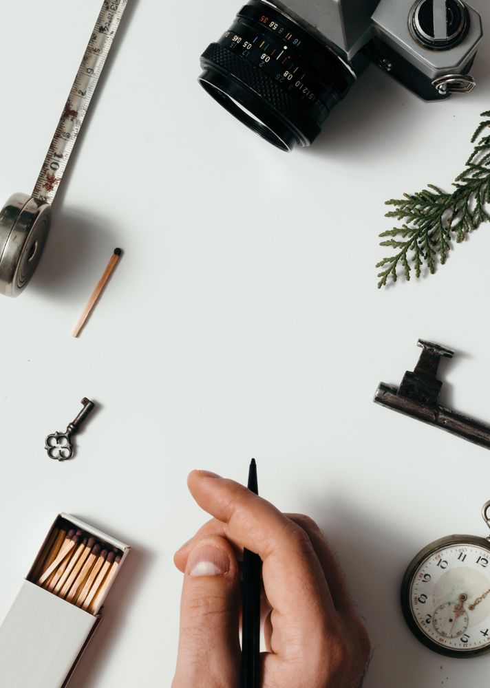 Hand holding pen above arrangement of vintage items on desk
