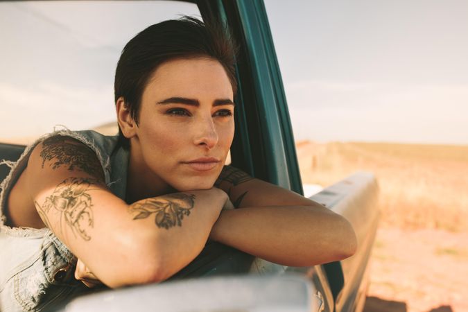 Ponderous woman resting head on crossed arms over open window of classic truck