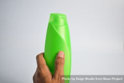 Hand holding mockup green shampoo bottle bxAA8d