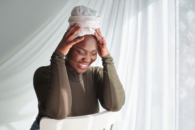 Cheerful woman in headwrap touching head and looking down