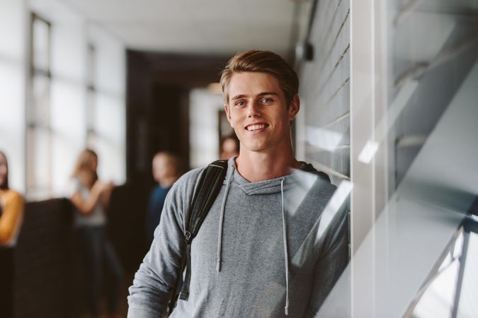 Portrait of teenage male student standing wall in corridor of a college