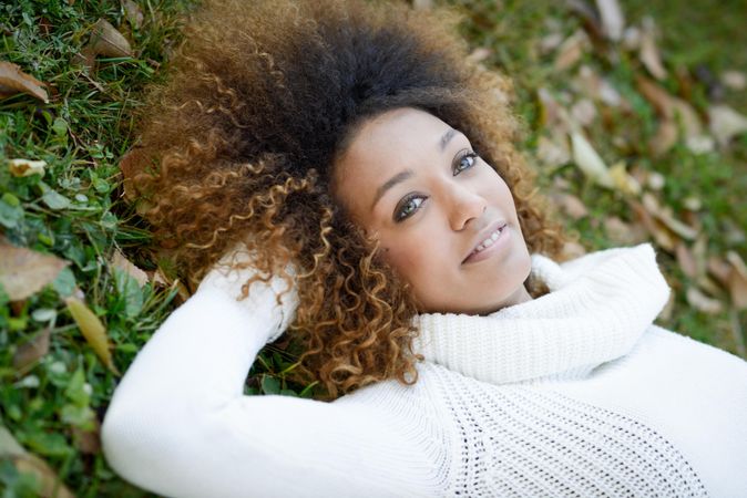 Happy female in sweater lying down on park grass