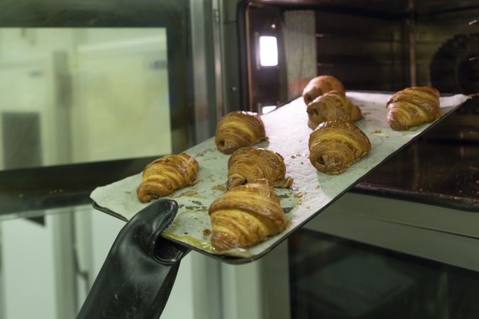 Cook holding baking tray with hot croissants