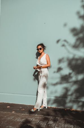 Woman in light jumpsuit in the sun in front of blue wall