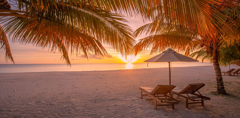 Wide shot of two lounger chairs on a beach as the sunsets