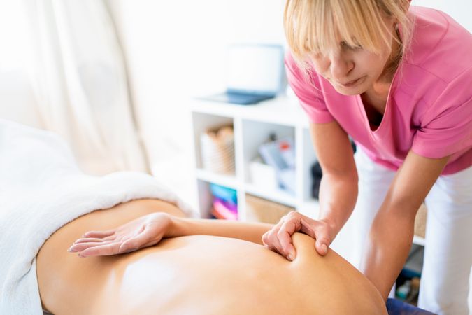 Masseuse massaging shoulder plades of woman in spa salon using fists