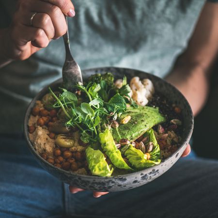 Woman in t-shirt and jeans sitting with fork in vegetarian bowl, square crop