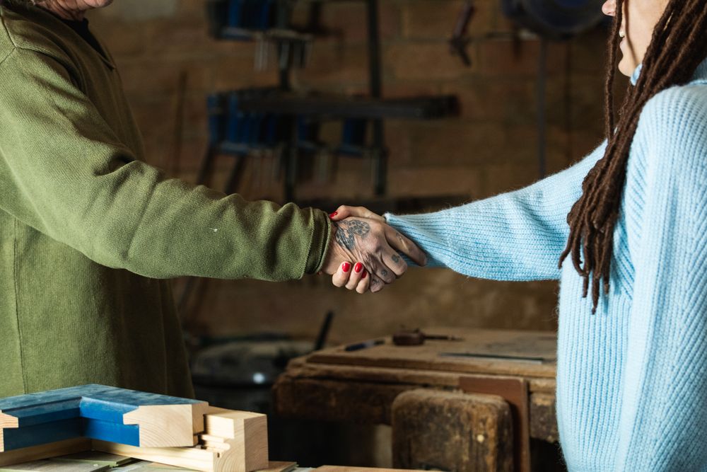Woman greeting woodworker with handshake in workshop