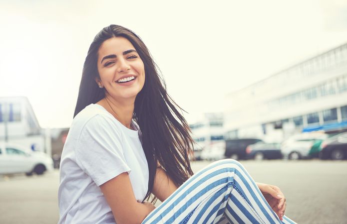 Woman sitting on the curb smiling with hair flowing in the wind