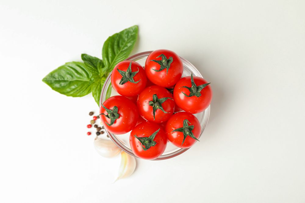 Bowl with fresh tomatoes, basil, garlic and pepper on plain background, space for text and top view