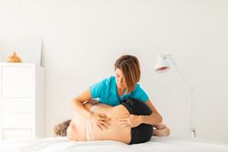 A female physical therapist performs a stretching and pressure exercise on her patient's lower back