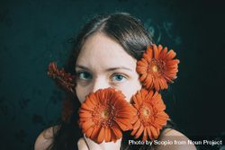 Studio portrait of woman with blue eyes holding orange flowers 48Elvb