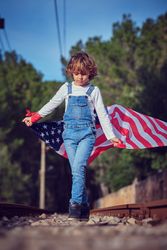 Kid on stones alongside railway with American flag