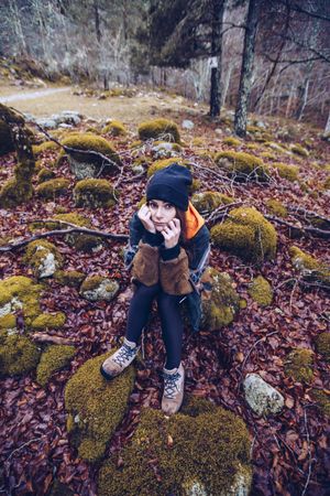 Bored female tourist resting on rock at autumn forest