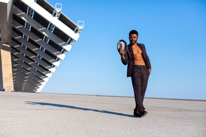 Front view of Black bearded man holding a hat while dancing against blue sky on a sunny day