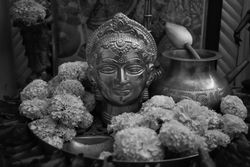 Grayscale photo of Buddha statue surrounded by marigold flowers on tray