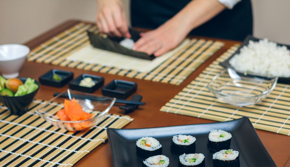 Hands of woman chef filling Japanese sushi rolls with rice on a nori seaweed sheet