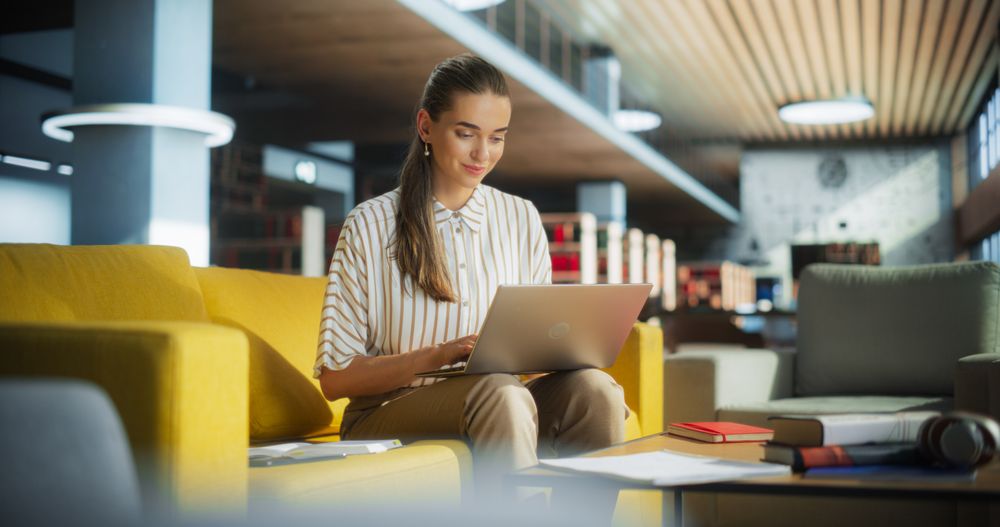 Young Female Specialist Working in a Rest Area in an International Startup Office. Manager Holding Her Laptop Computer on a Lap, Browsing Internet, Researching Project Information Online