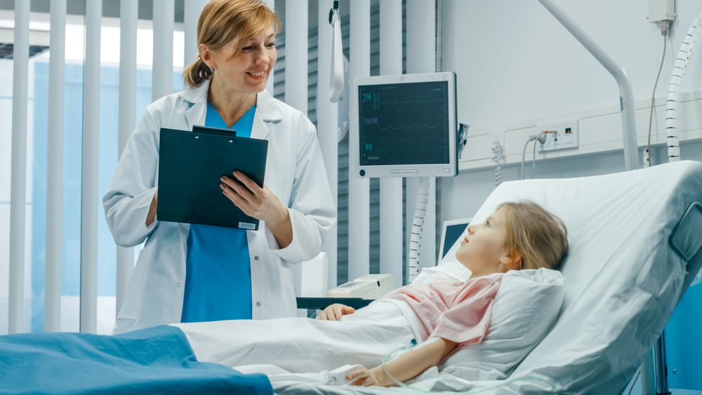 Recovering Little Girl Lies on a Bed In the Hospital, Friendly Doctor With Clipboard Asks Questions