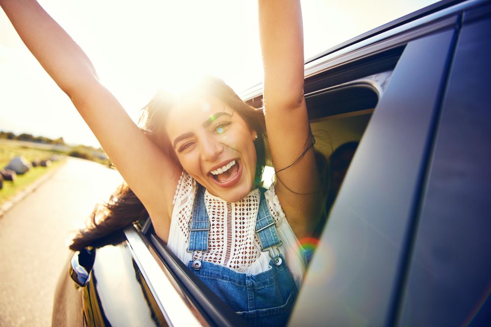 Smiling woman with arms outstretched in celebration outside of car window