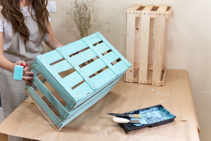 Woman paining wooden box in blue color with roller