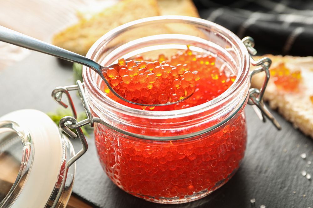 Composition with caviar in glass jar, bread, spoon, towel and cutting board, space for text