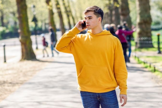 Man in yellow hoodie talking on cell phone while walking in park
