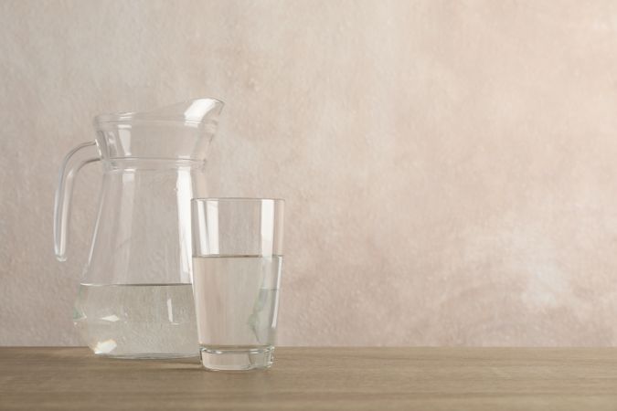 Pitcher of water with glass in beige room with copy space