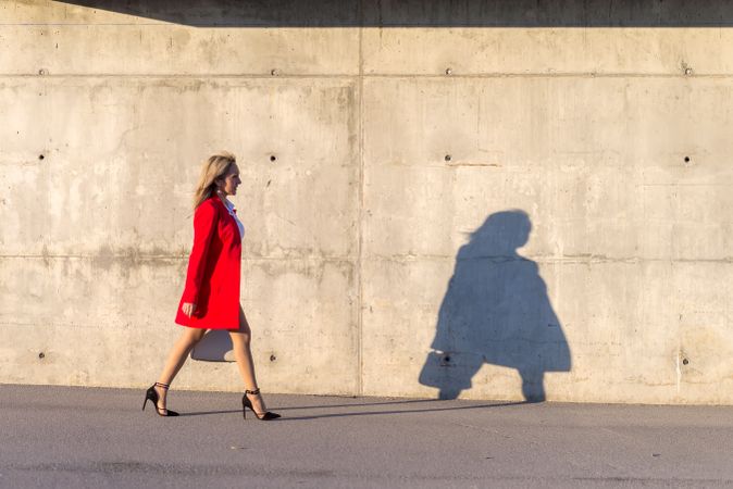Businesswoman wearing red jacket walking on the street with long shadow