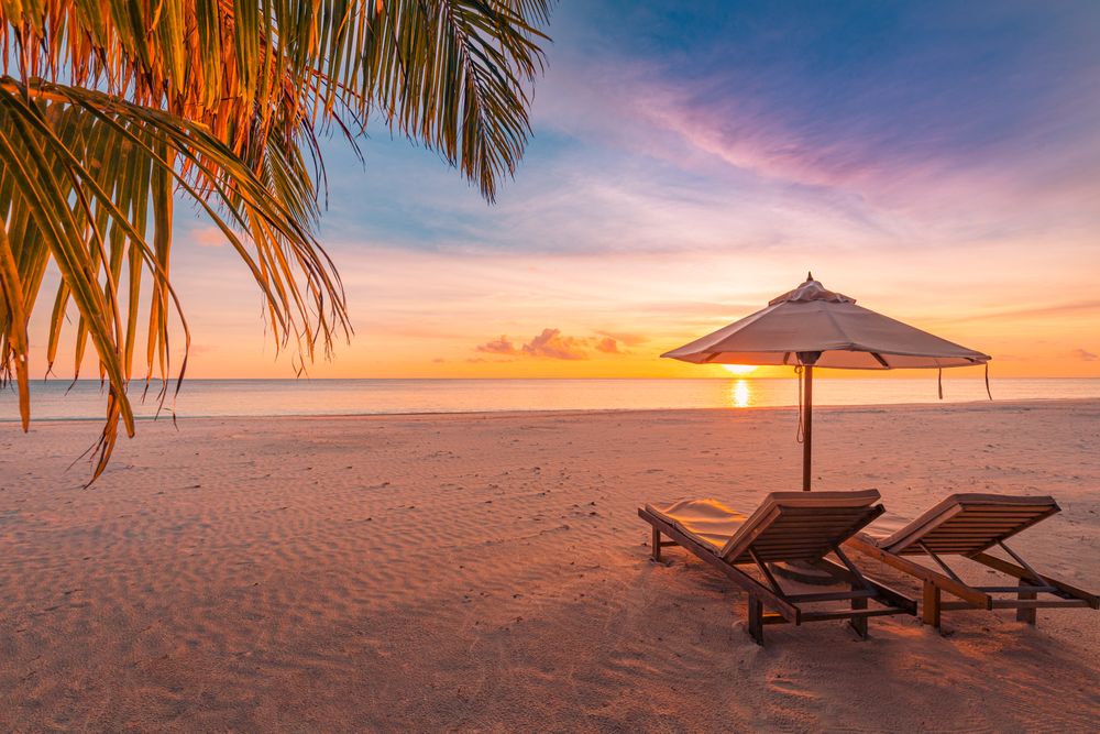 Two relaxing beach chairs with umbrella at the beach at sunset