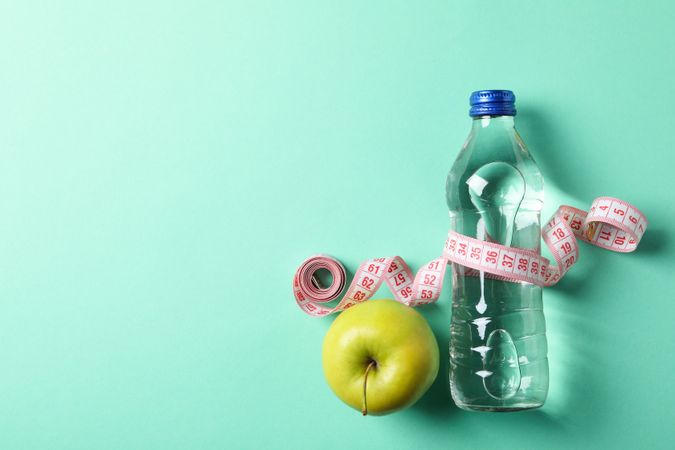 Bottle of water, measuring tape and apple on mint background