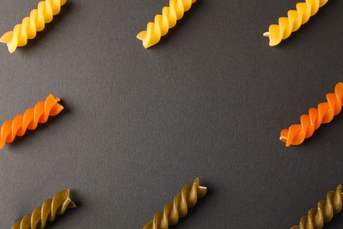 Flat lay composition with multicolored pasta on dark background, space for text and closeup