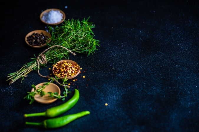 Pepper, herbs, oil and seasoning on dark counter with copy space