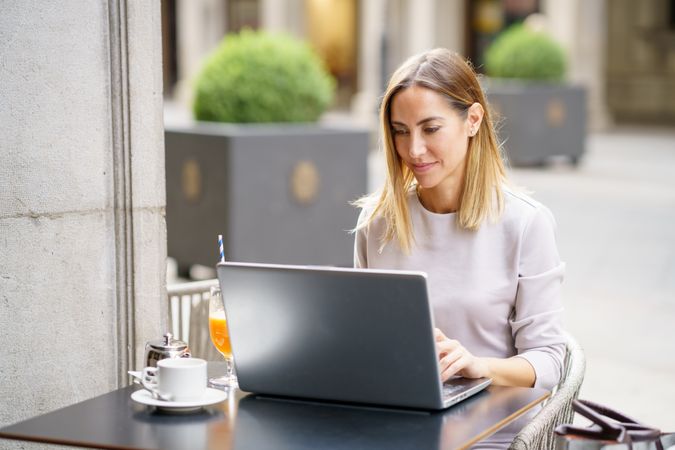 Woman in grey sitting in cafe outside with laptop