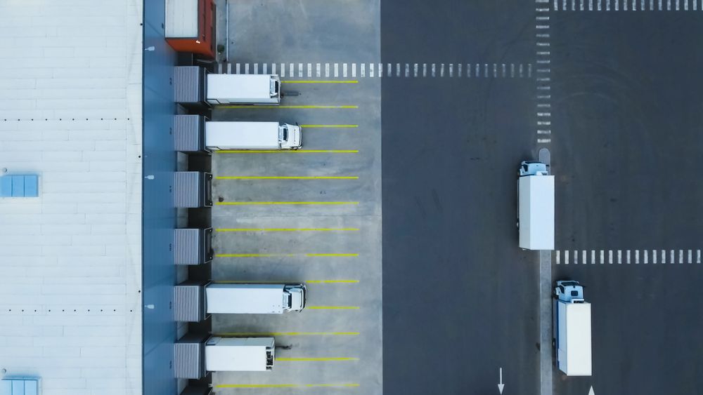 Aerial Side Shot of Industrial Warehouse Loading Dock where Many Truck with Unload Merchandise.